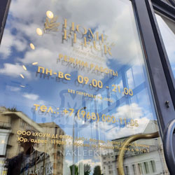 Золотистые буквы с графиком работы на стекле двери магазина цветов